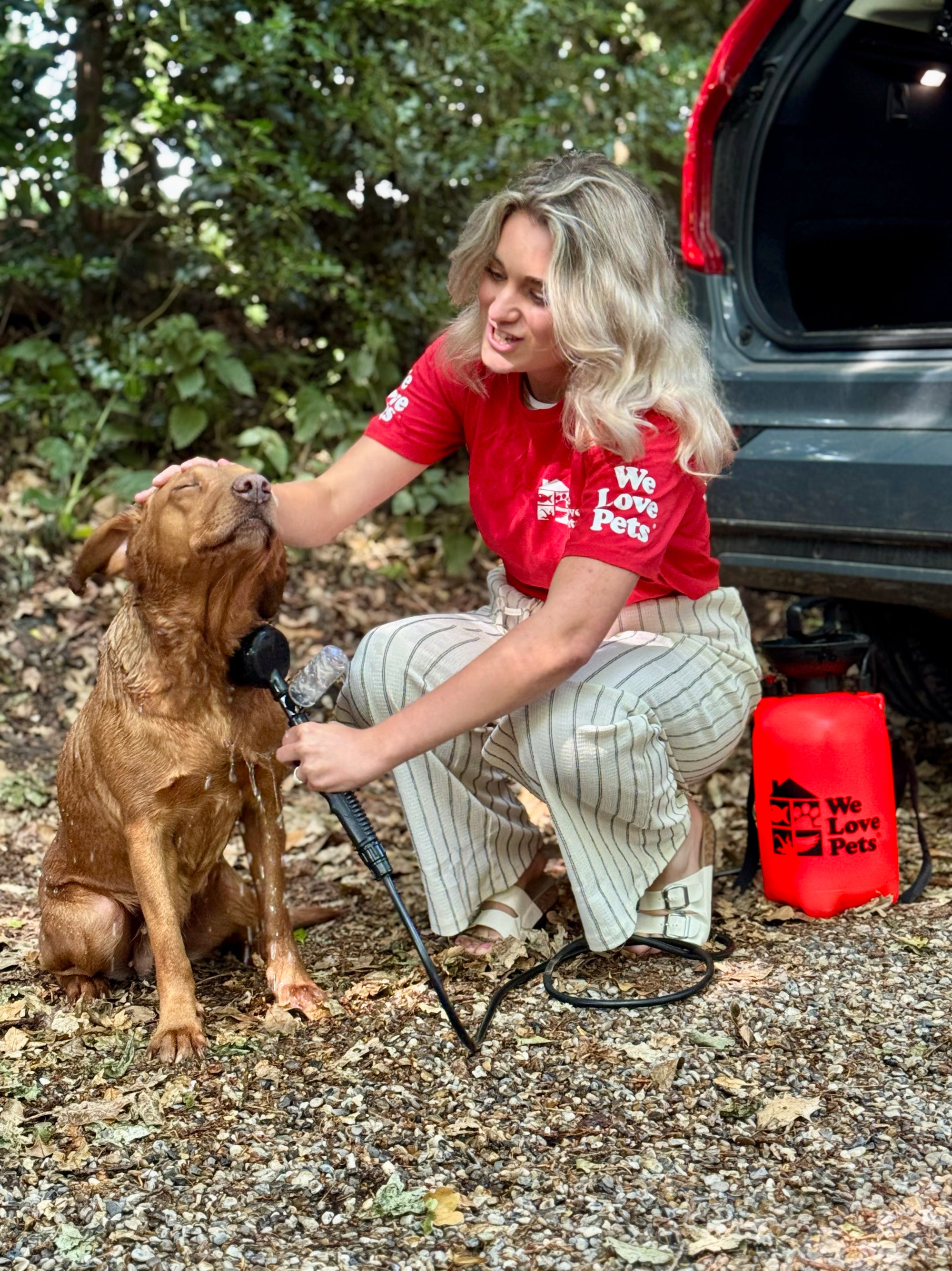 Dog owner using We Love Pets Portable Paw Washer to clean muddy paws outdoors